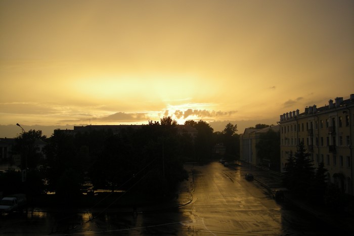 Sunset over a wet city street with buildings and trees