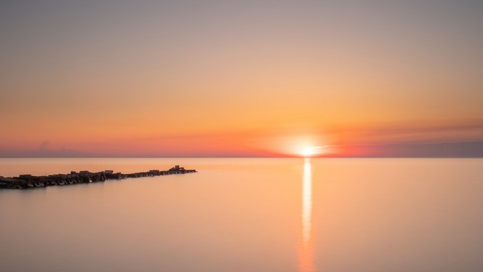 Sunset over calm water with breakwater