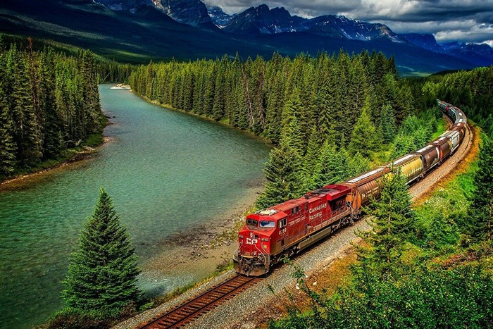 Canadian Pacific train by a river in a forest with mountains