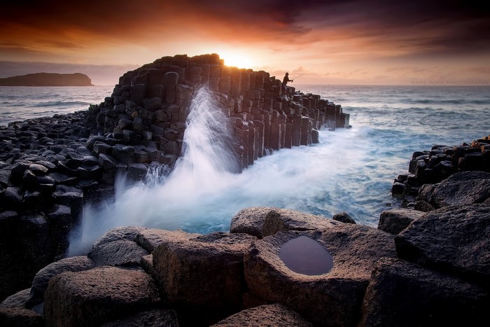 Person fishing on basalt columns at sunset
