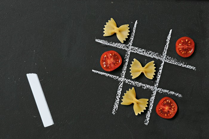Tic-tac-toe game with pasta and tomatoes on chalkboard