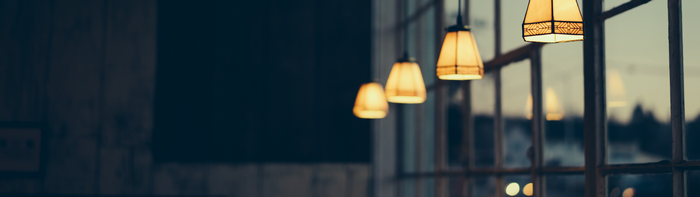 Four pendant lights hanging in front of a window at dusk