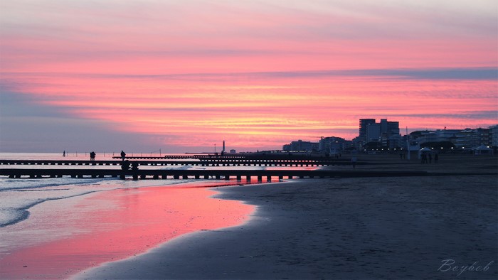 Sunset over a beach with a pier and city skyline