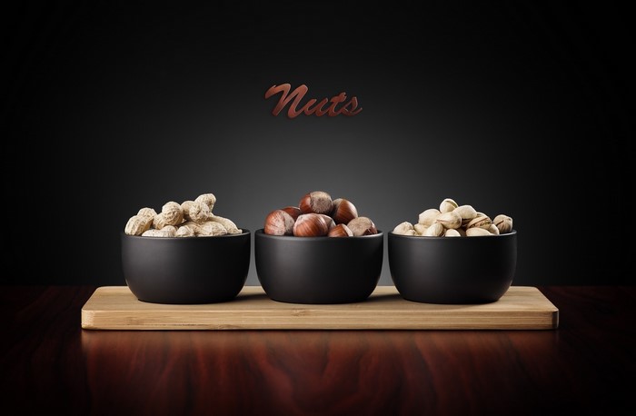 Three bowls of nuts on a wooden board