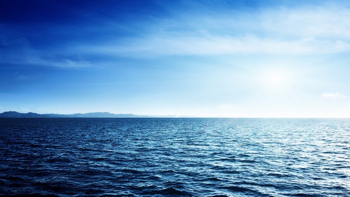 Ocean horizon with distant mountains and blue sky