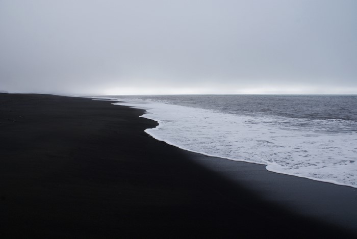 Black sand beach with waves under overcast sky