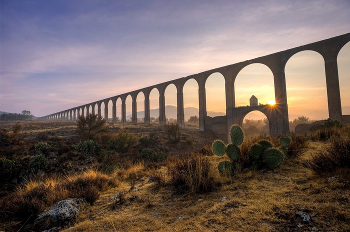 Aqueduct arches at sunrise with sun rays and cacti