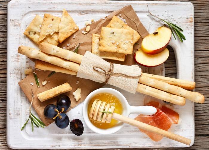 Appetizer platter with breadsticks, grapes, apples, and prosciutto