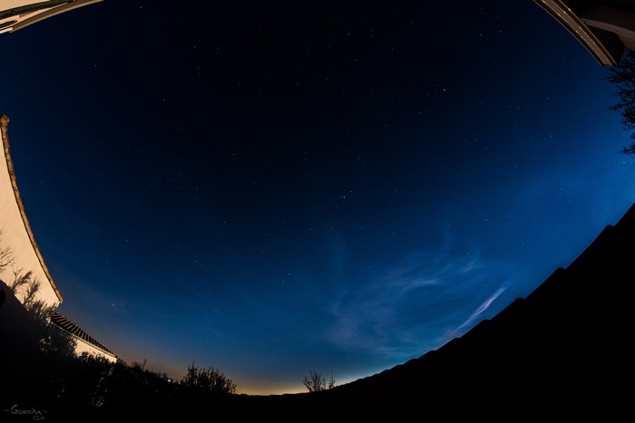 Night sky with stars and clouds over a silhouette of buildings and trees