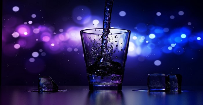 Dark liquid being poured into a glass with ice cubes
