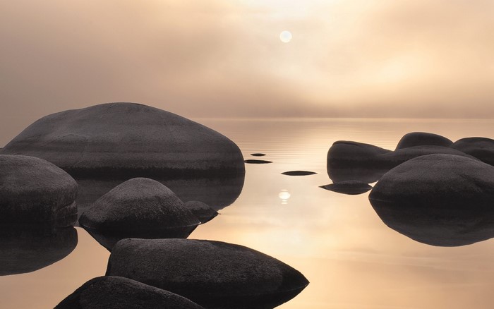 Misty landscape with rocks and sun reflection on water