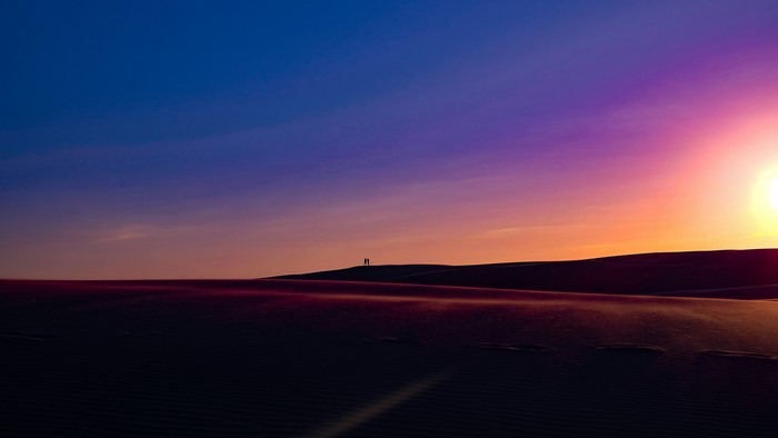 Two people silhouetted on a sand dune at sunset