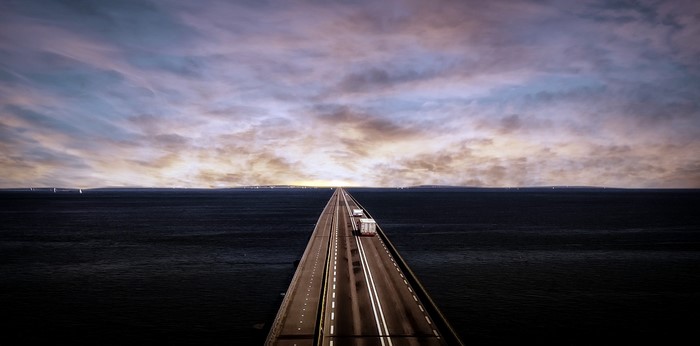 Bridge over the ocean at sunset with trucks