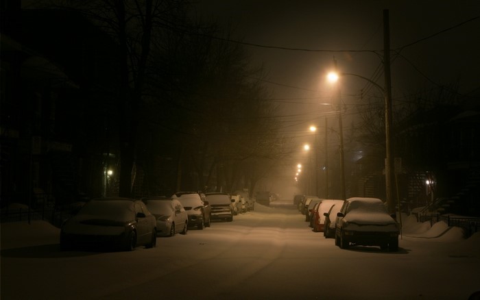 Snowy street at night with street lights and parked cars