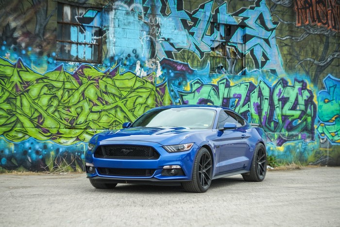Blue Ford Mustang parked in front of graffiti wall