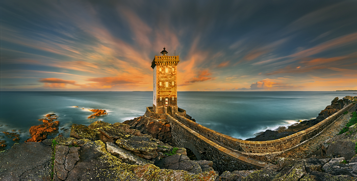 Lighthouse on a rocky coast with dramatic sunset sky