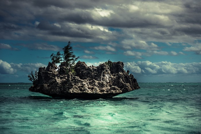 Rock island with trees in the sea under clouds