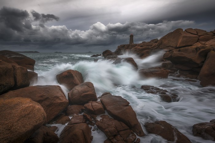 Lighthouse on rocky coast with crashing waves