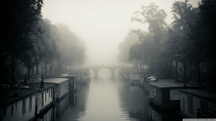 Misty canal with houseboats and a bridge