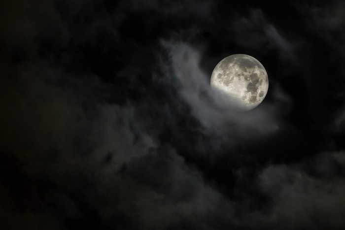 Full moon obscured by dark clouds at night