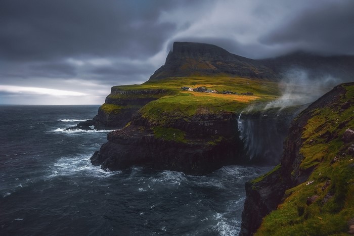 Waterfall cascading from cliffs into the sea under a cloudy sky