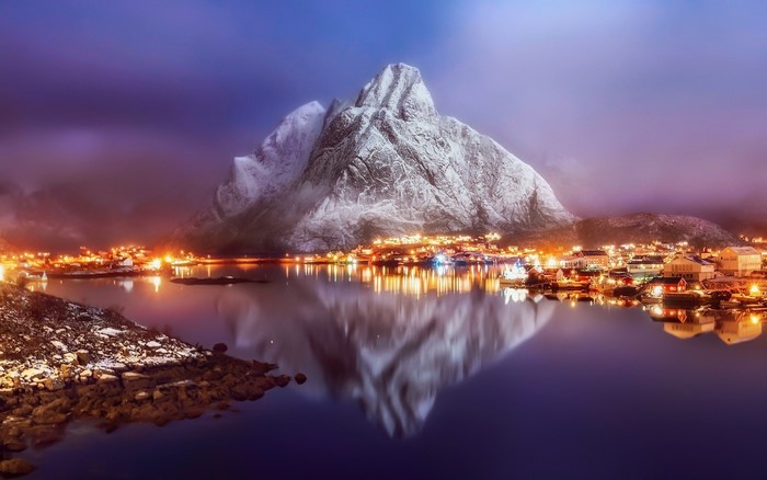 Town lights reflecting on water with snowy mountain
