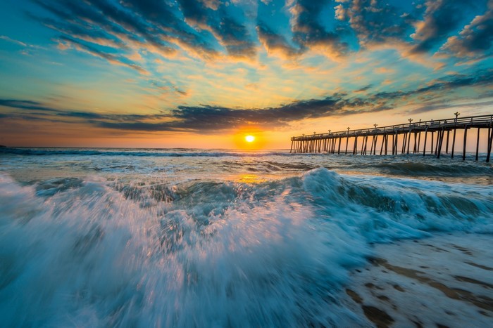 Sunrise over the ocean with a pier and waves