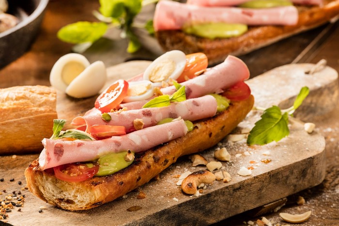Sandwich with ham, eggs, tomatoes, and avocado on a baguette