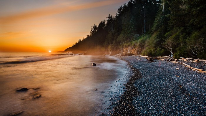 Sunset over a rocky beach with a forest