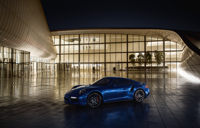 Blue Porsche 911 Turbo S parked at modern building at night