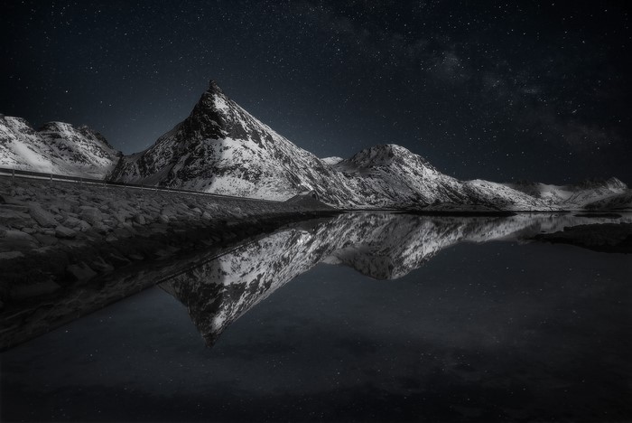 Snowy mountains reflected in water under starry night sky
