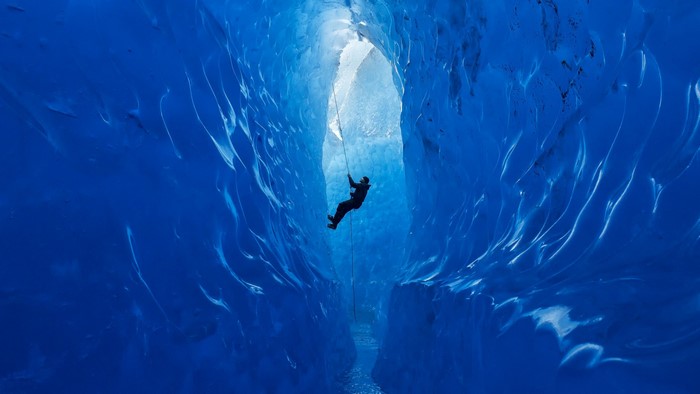 Person rappelling down a blue ice cave