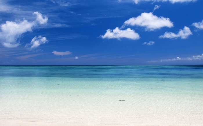 Clear turquoise ocean water and white sand beach under blue sky with clouds