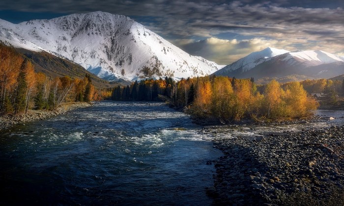 River flowing past autumn trees towards snow-capped mountains
