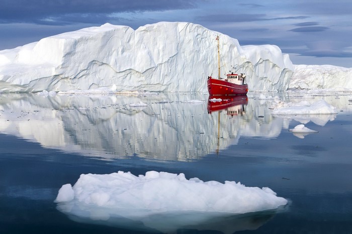 Red boat near a large iceberg in the Arctic