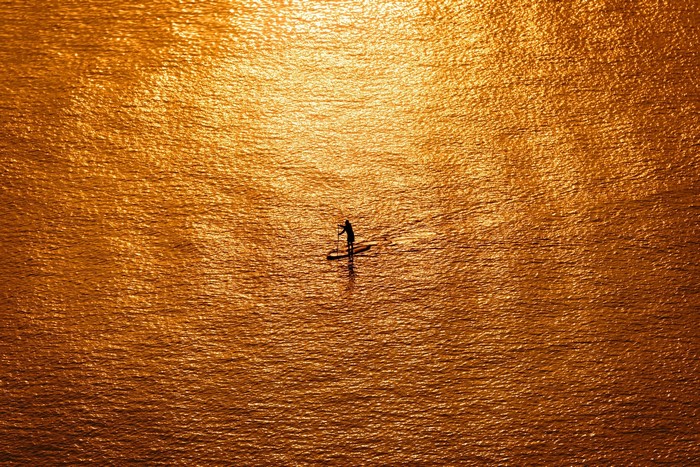 Person paddleboarding on orange water at sunset
