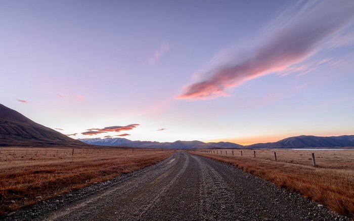Dirt road through plains at sunset with mountains