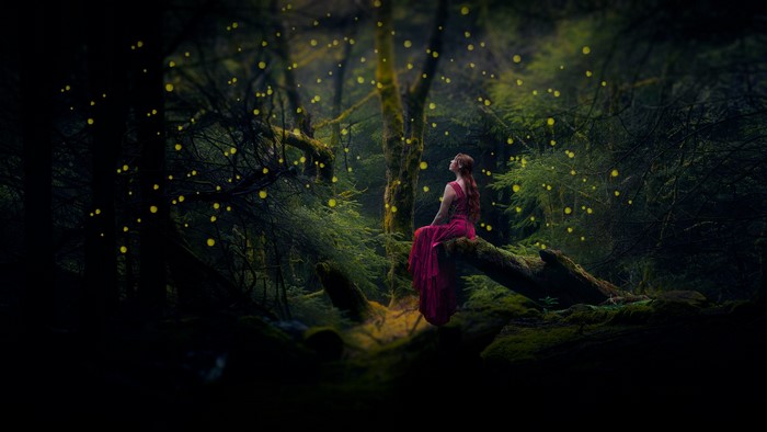 Woman in red dress in a magical forest with glowing lights