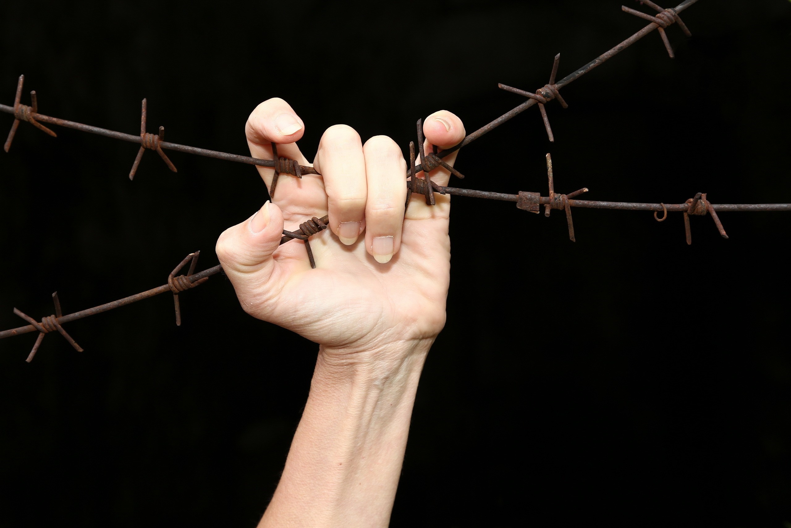 Hand gripping barbed wire against black background HD Wallpaper