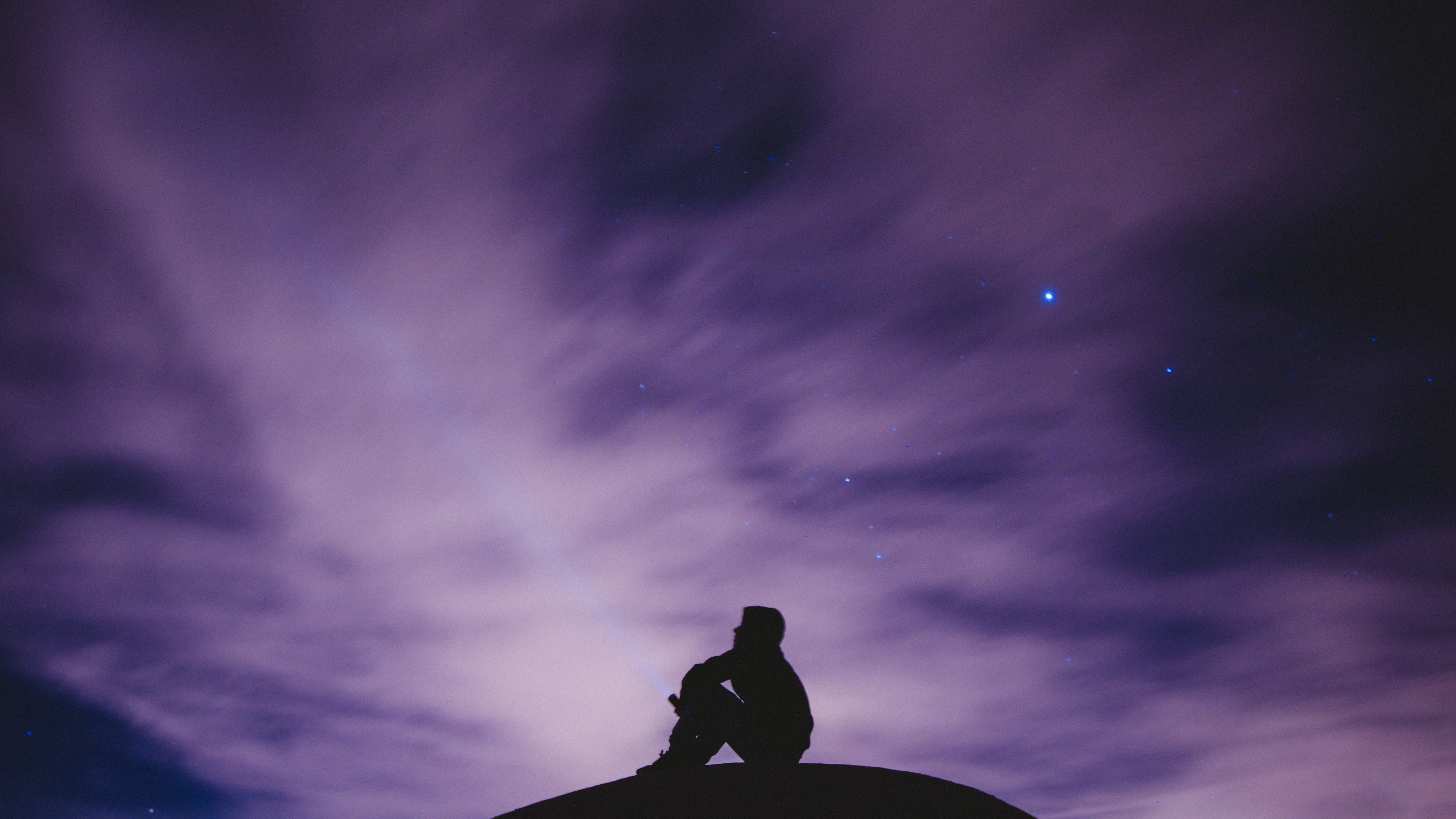 Silhouette of a person sitting under a starry purple sky HD Wallpaper