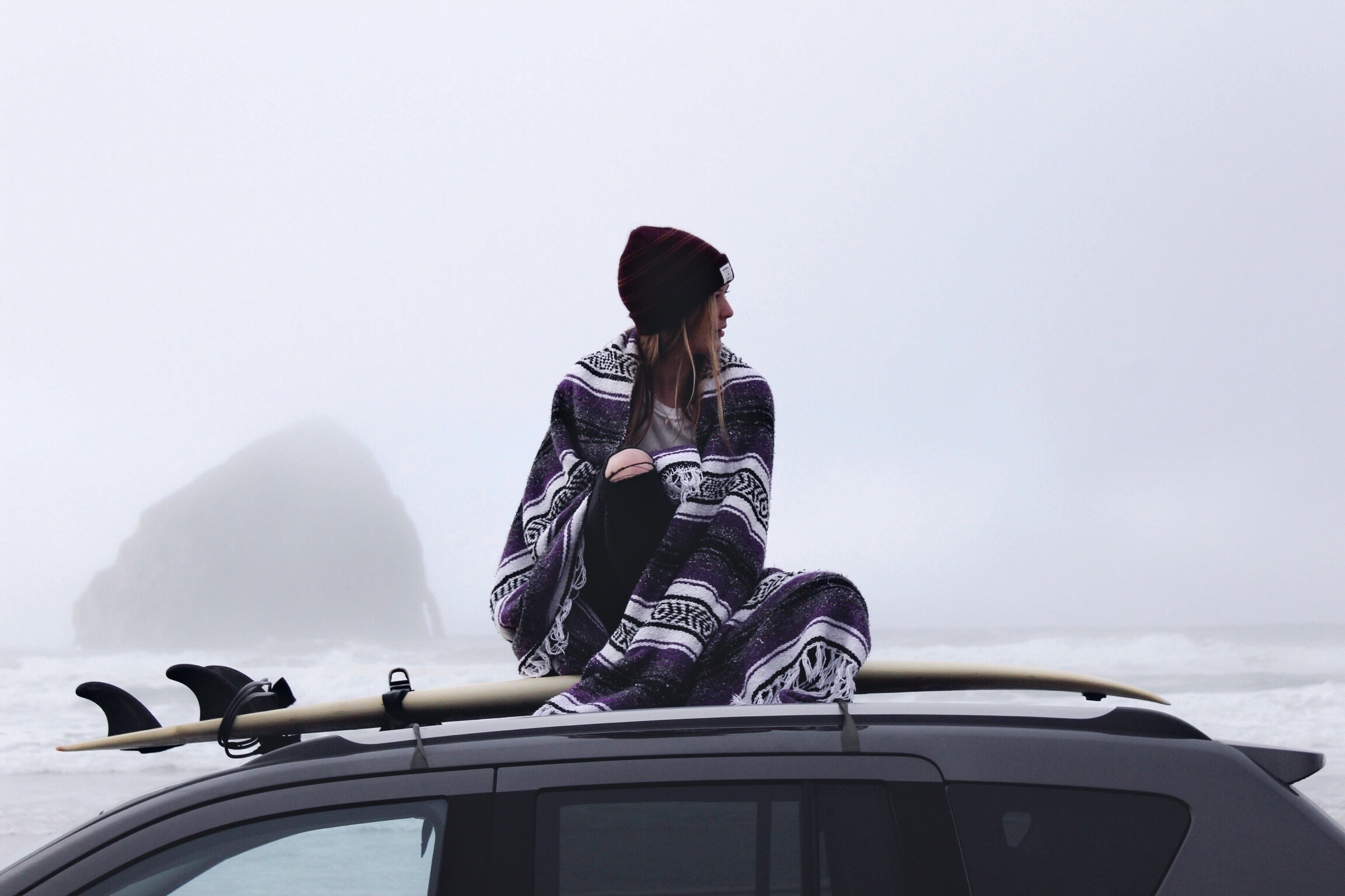 Woman wrapped in blanket on car roof with surfboard HD Wallpaper