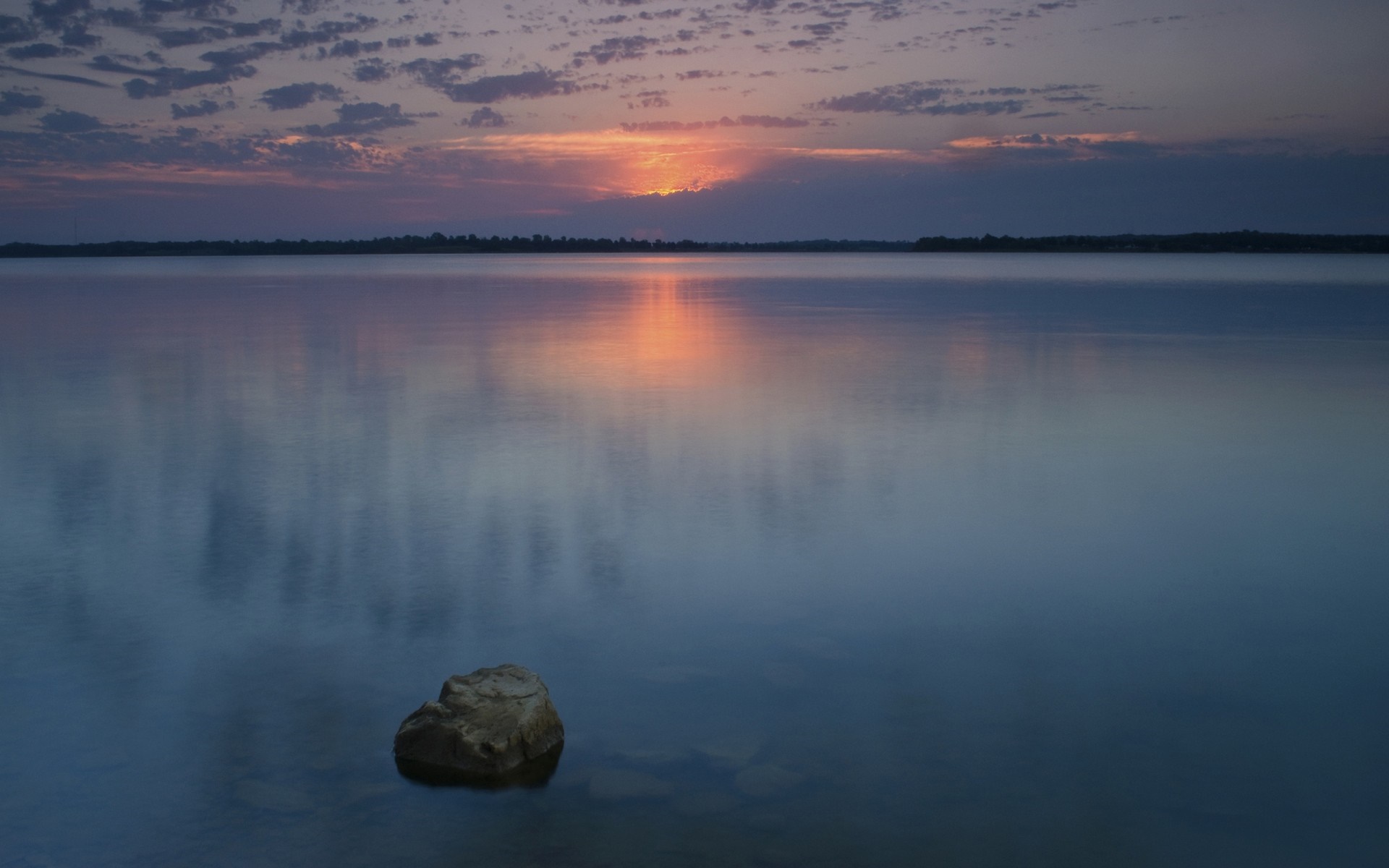 Sunset over a calm lake with a rock in the foreground HD Wallpaper