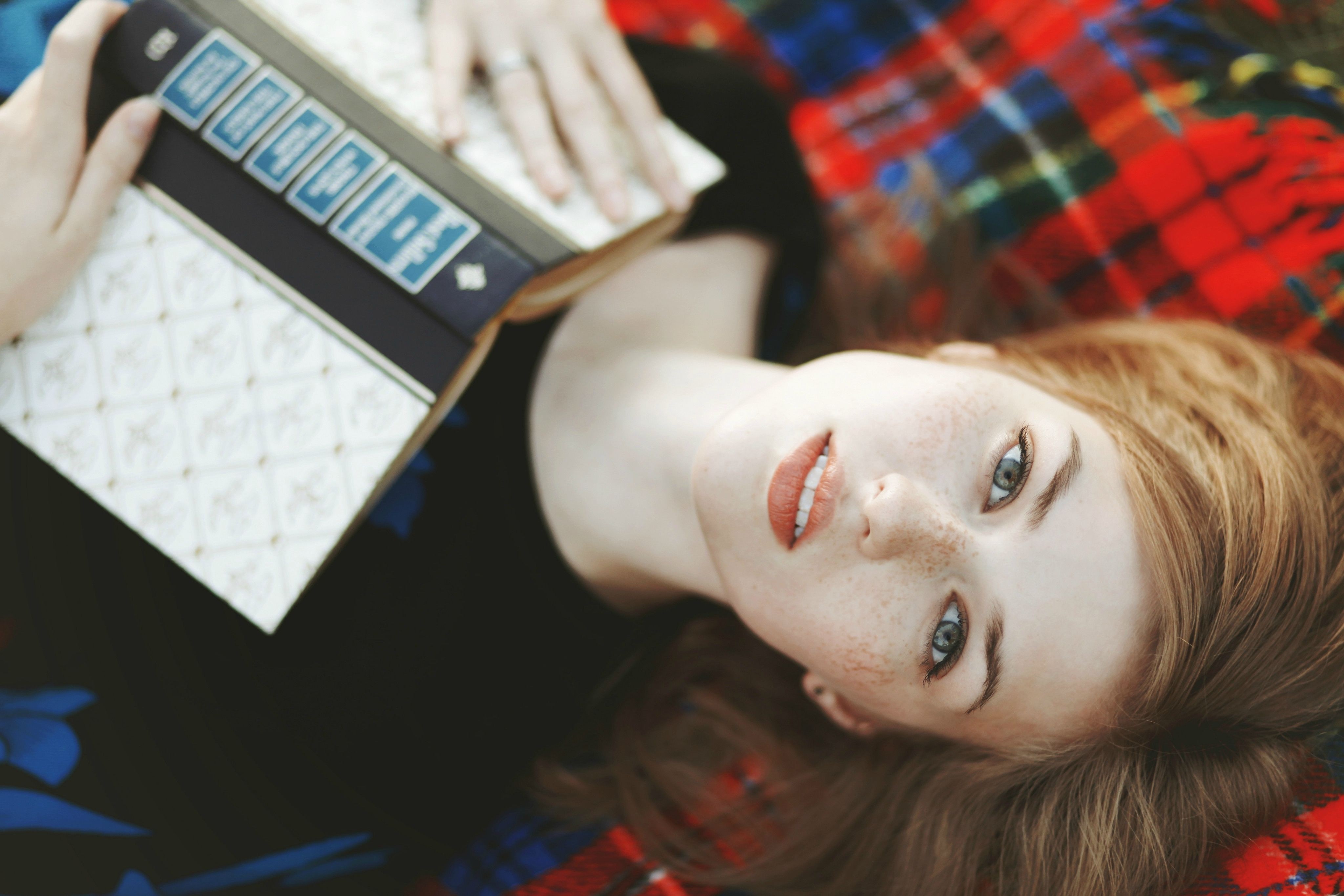 Woman with book lying on a plaid blanket HD Wallpaper