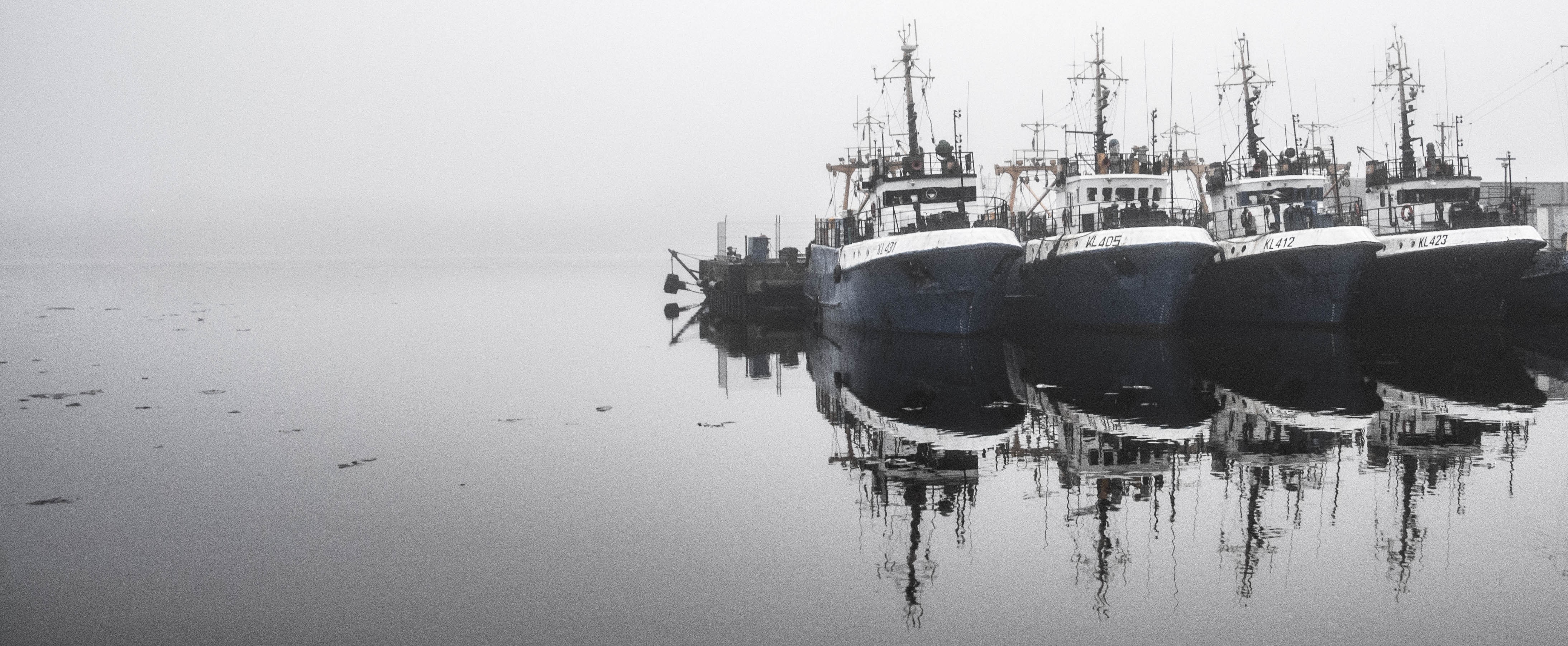 Fishing boats docked in a foggy harbor with reflections HD Wallpaper