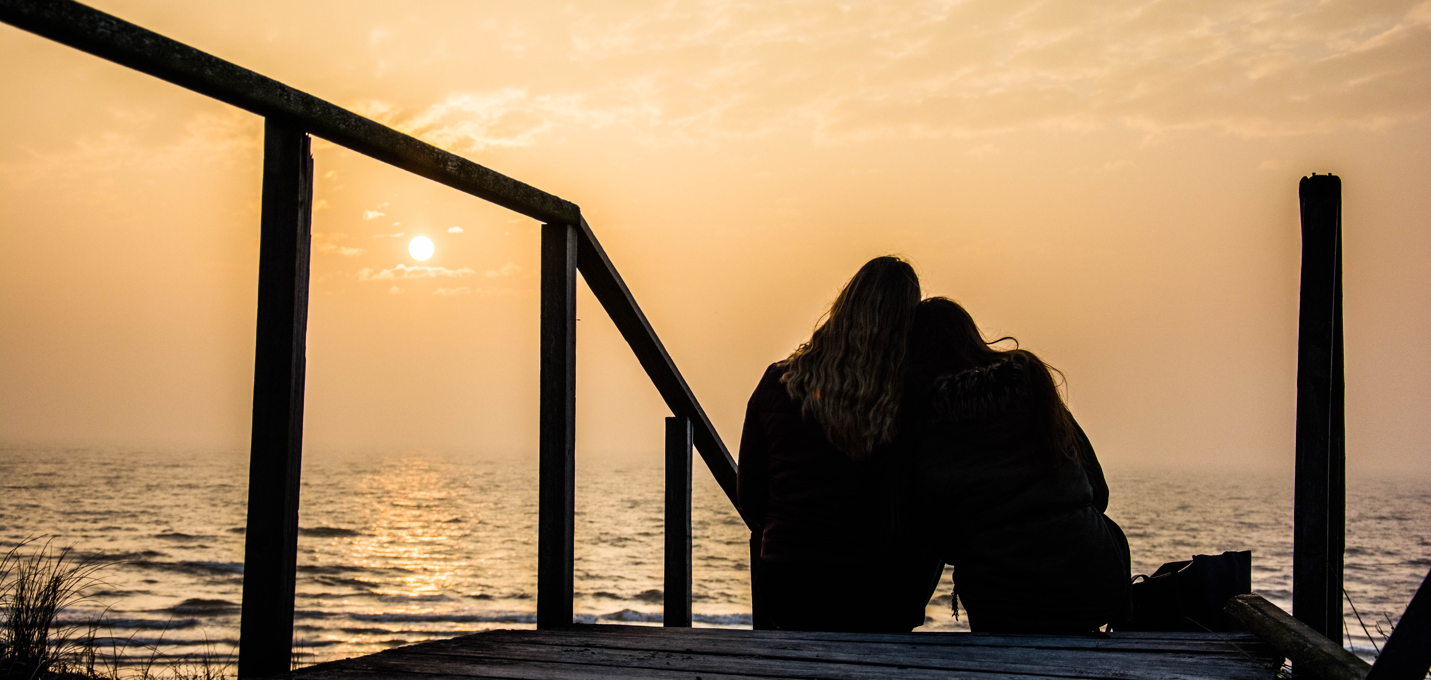 Two people silhouetted on a wooden deck at sunset HD Wallpaper