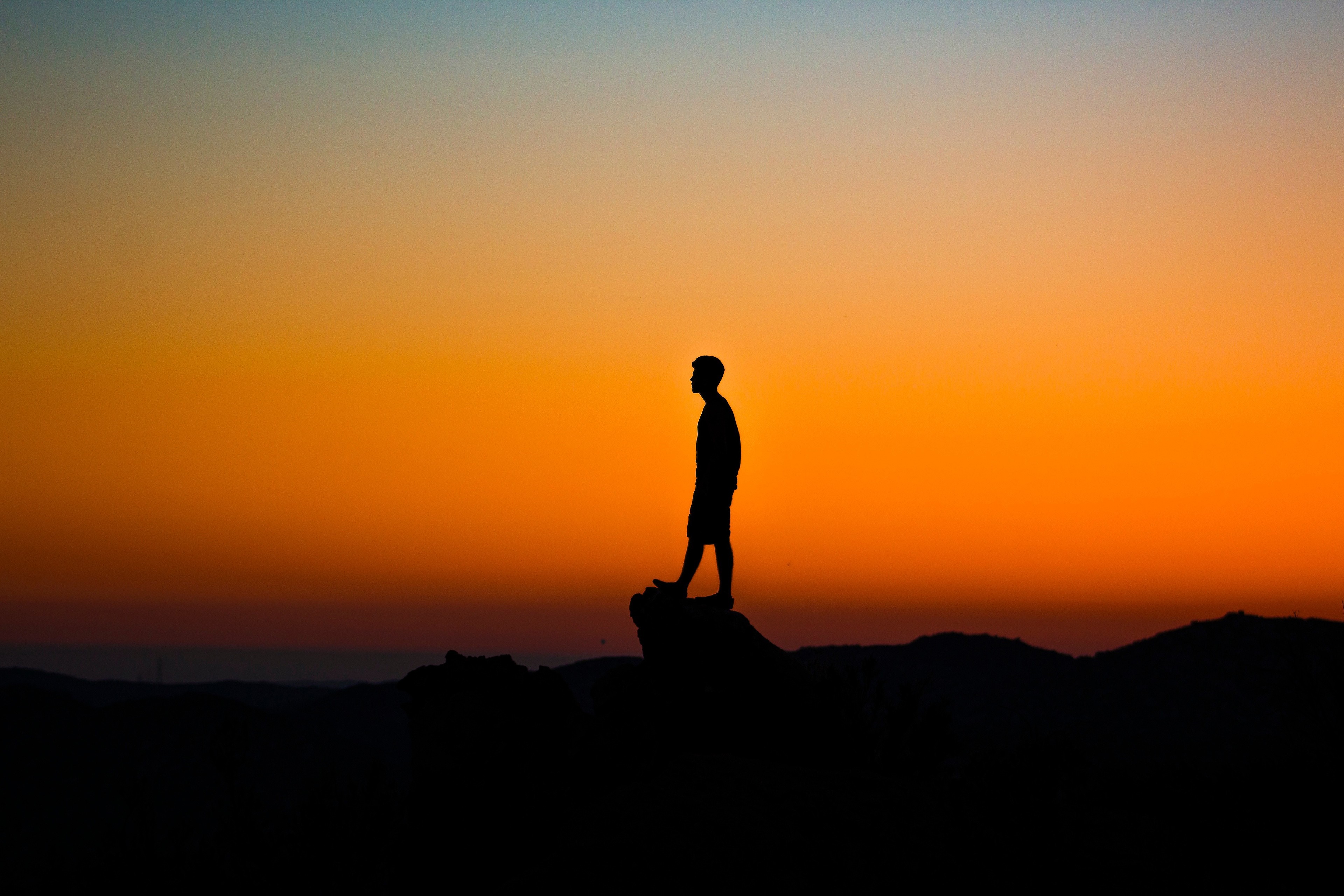 Silhouette of a person standing on a rock at sunset HD Wallpaper