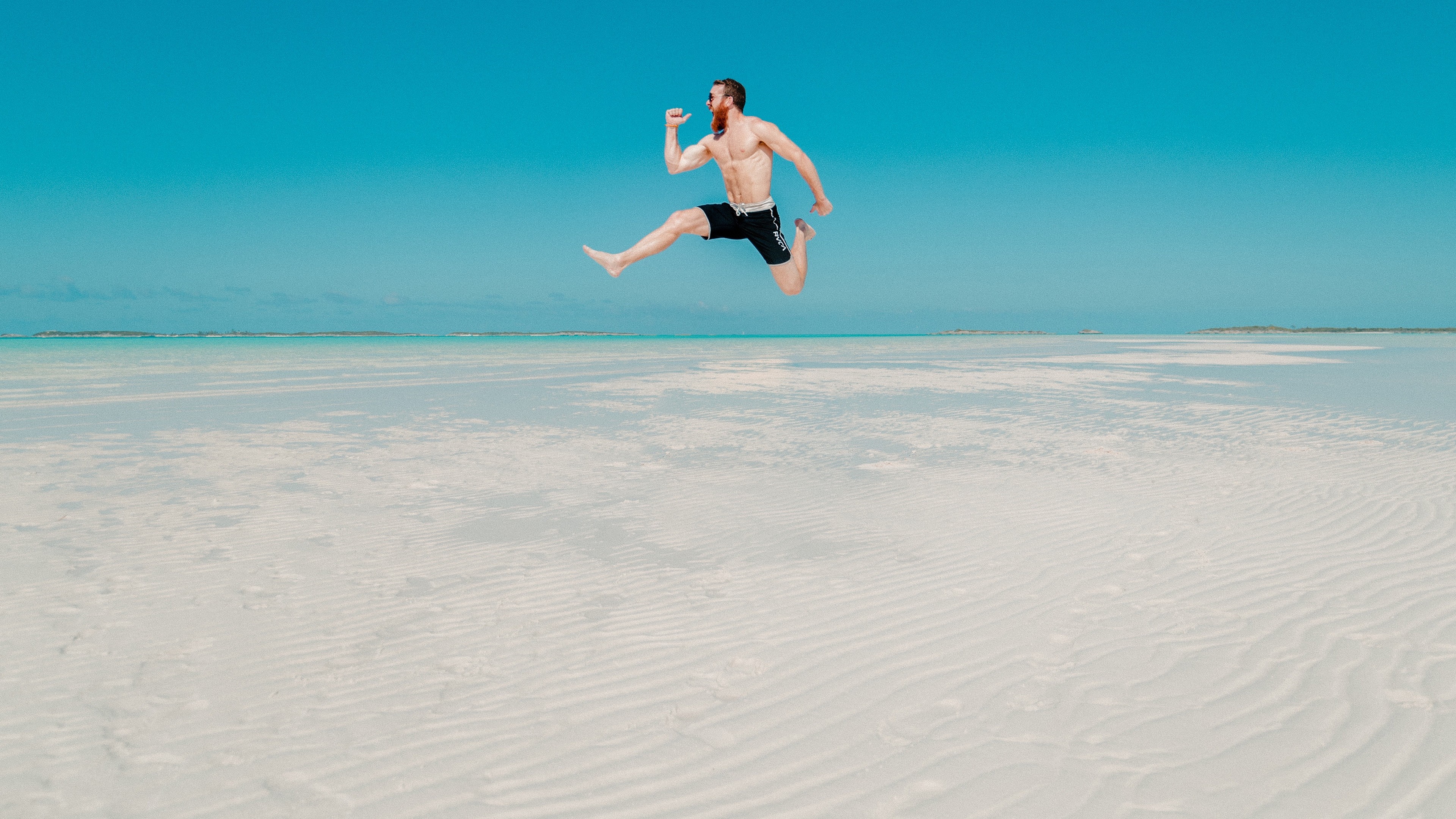 Man jumping on a beach with clear blue sky HD Wallpaper