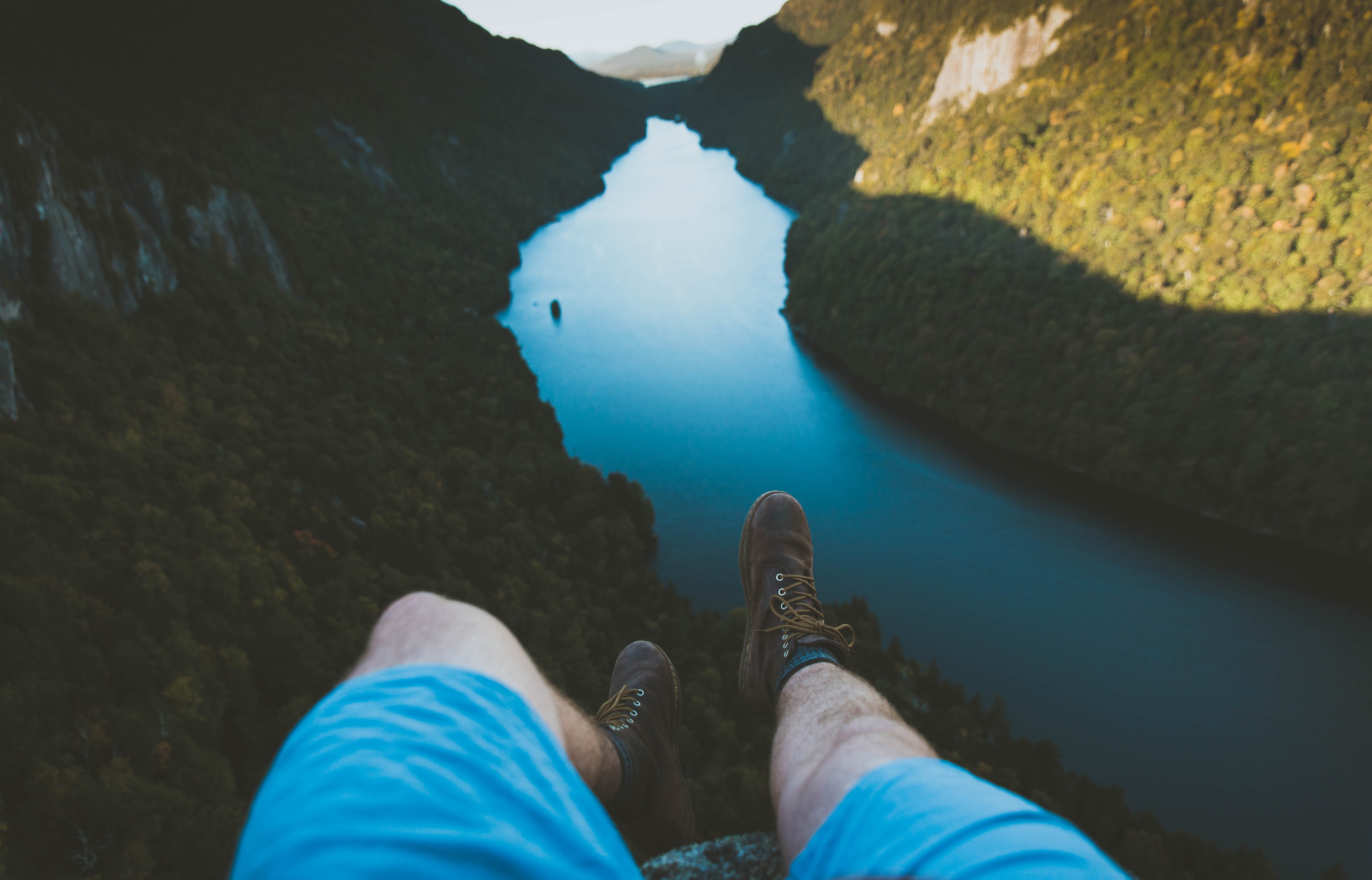 Person sitting on cliff edge overlooking a lake HD Wallpaper