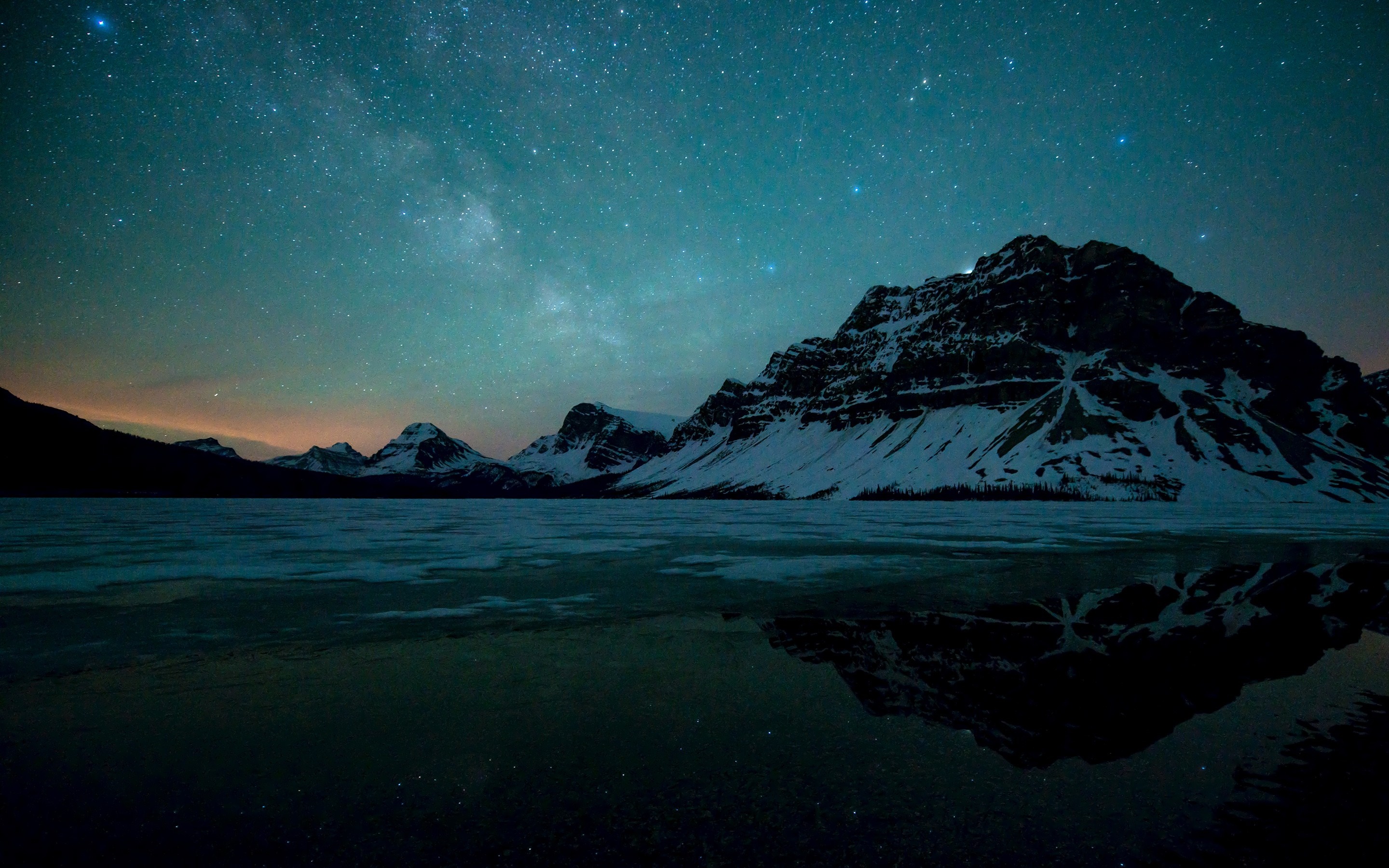Snowy mountains reflected in a frozen lake under a starry night sky HD Wallpaper