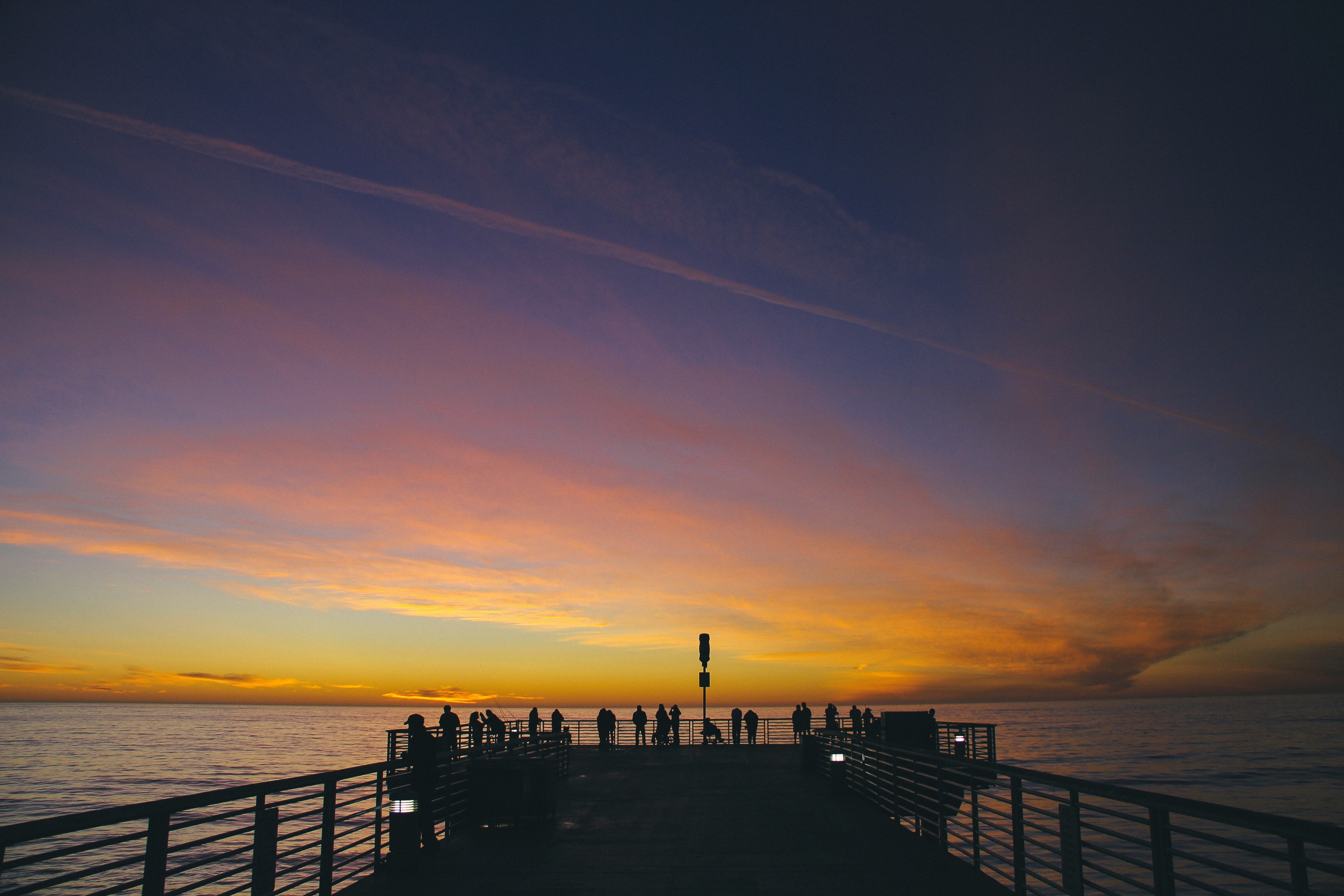 People on a pier watching a sunset over the ocean HD Wallpaper